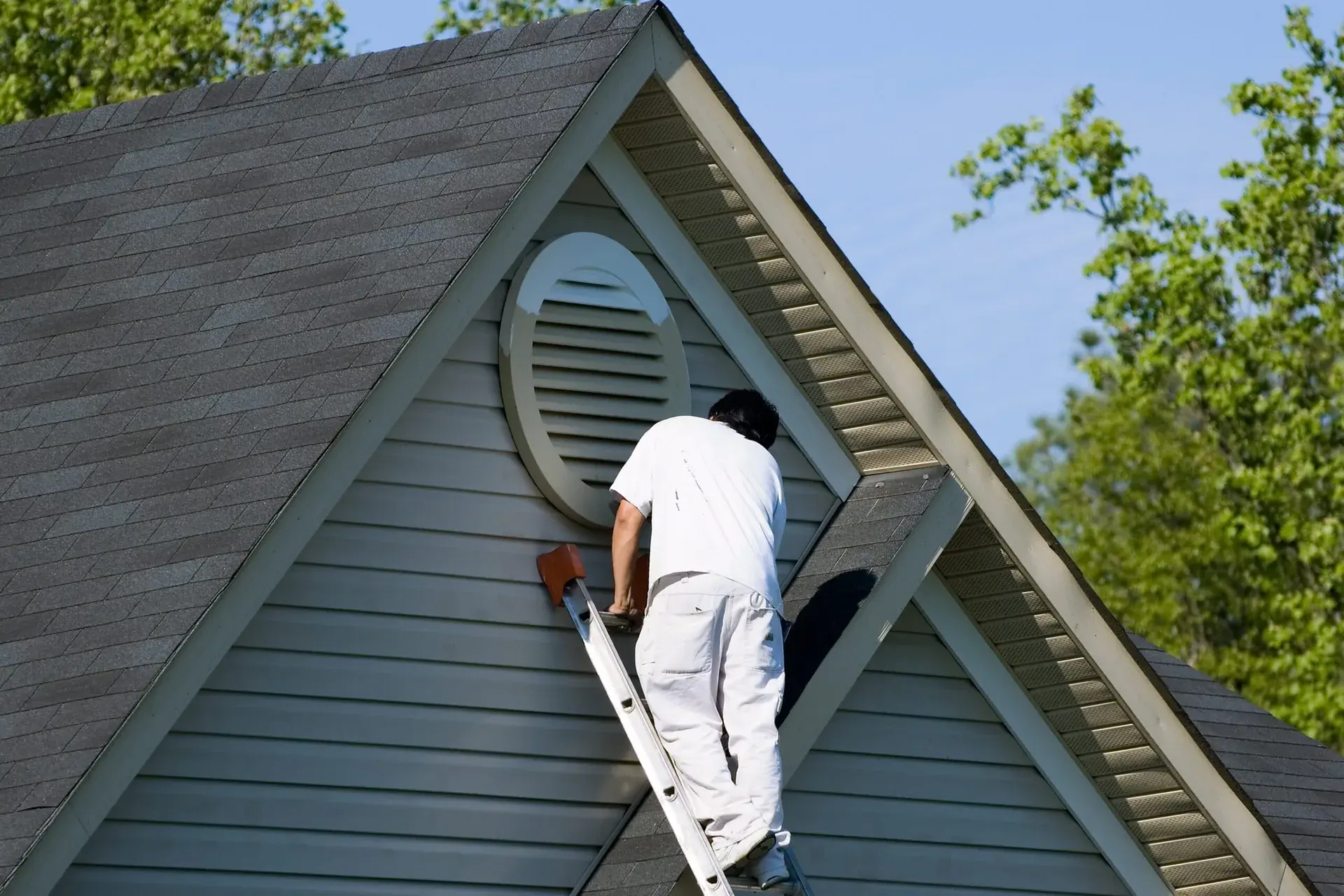 Painter on a ladder painting the gable end of a home